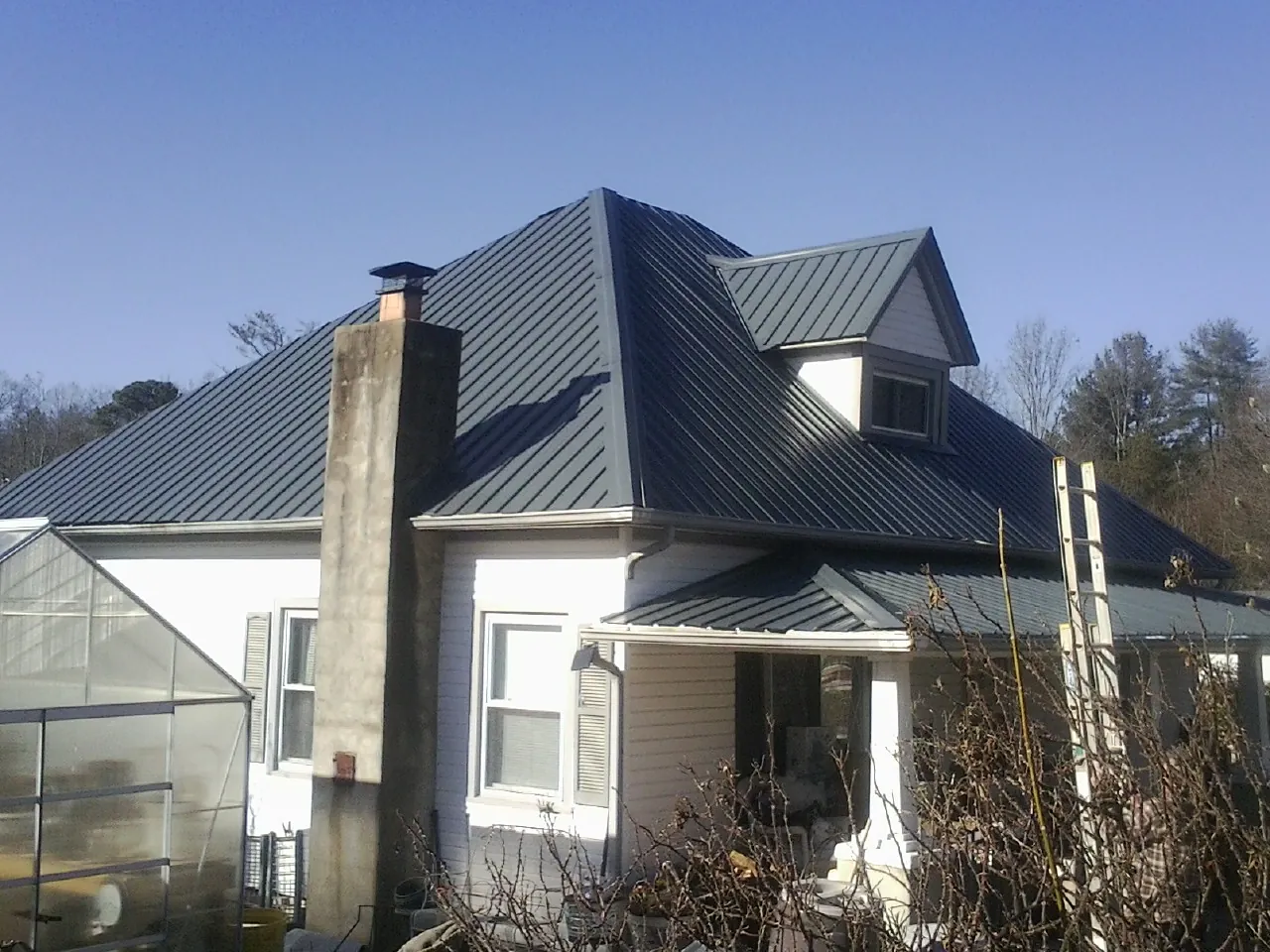 Dark blue standing seam metal roof on a white farmhouse with dormer — Slate & Tile Roof Repair by Roofing Brothers in Clarksburg