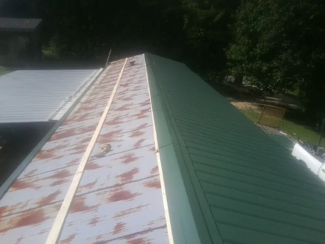 Old rusted panels beside newly installed green metal roofing — Wind Damage Roof Repair by Roofing Brothers in Clarksburg