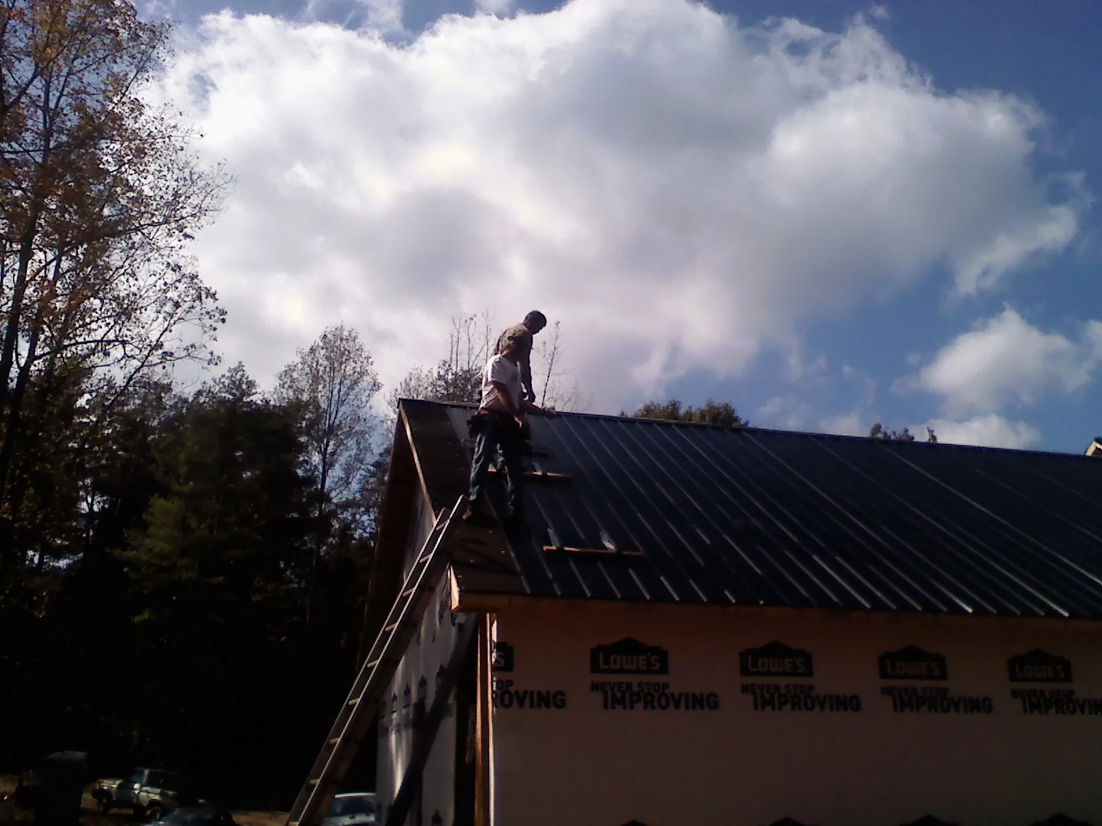 Roofer fastening dark metal panels high against a cloudy sky, from a Roof Inspection job in Clarksburg