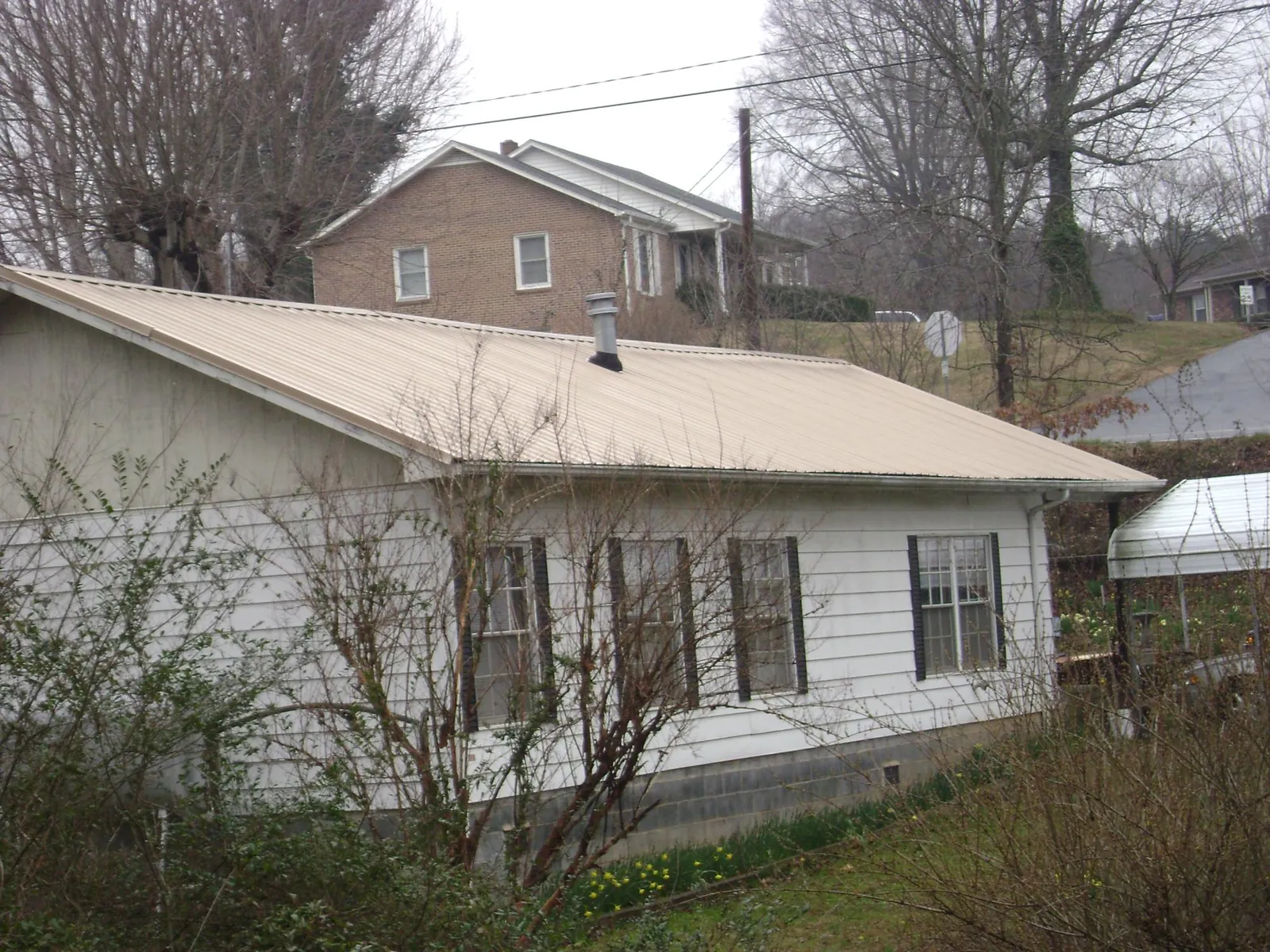 Tan metal roof on a white sided house set into a hillside — Commercial Roofing by Roofing Brothers in Clarksburg